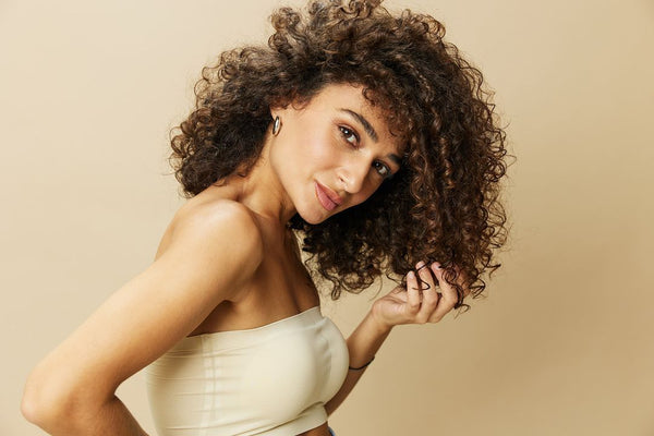 Beautiful woman with voluminous, healthy and well-maintained curly hair, emphasizing the importance of proper care in preventing hair loss and promoting natural hair growth.